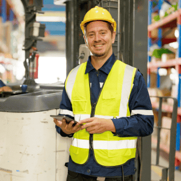 Worker in high-visibility vest using a tablet for logistics safety management inside a warehouse.