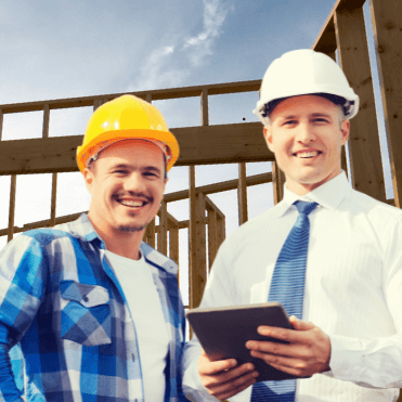 Two residential builders wearing safety helmets reviewing safety documentation on a digital tablet at a residential construction site, illustrating safety software for residential builders.