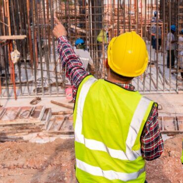 An authoritative supervisor in a yellow hard hat and safety vest points toward an unauthorised person entering a construction zone, highlighting the strict enforcement of contractor site access and safety protocols on a busy work site.