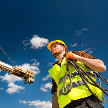 UK construction worker wearing PPE beside a crane, using safety software tools to support site compliance, risk management and worker safety.
